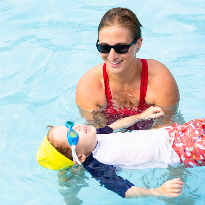 Swim instructor helping little boy swim.