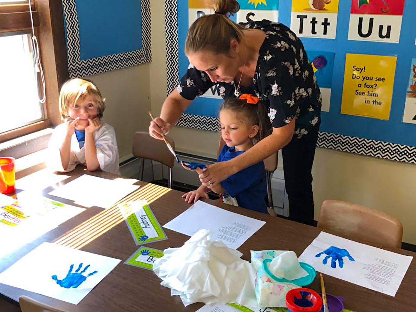 Teacher helping student paint her hand.