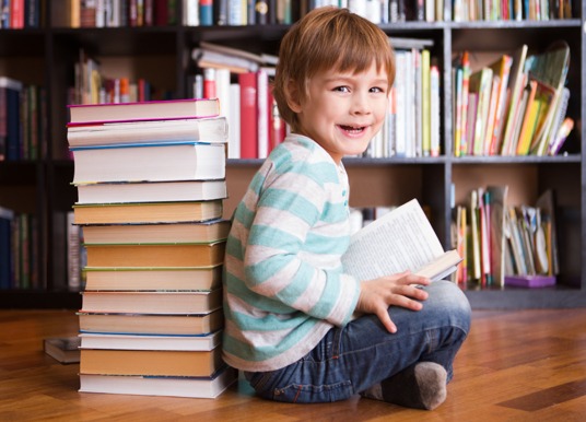 Boy toddler reading a book in a library.